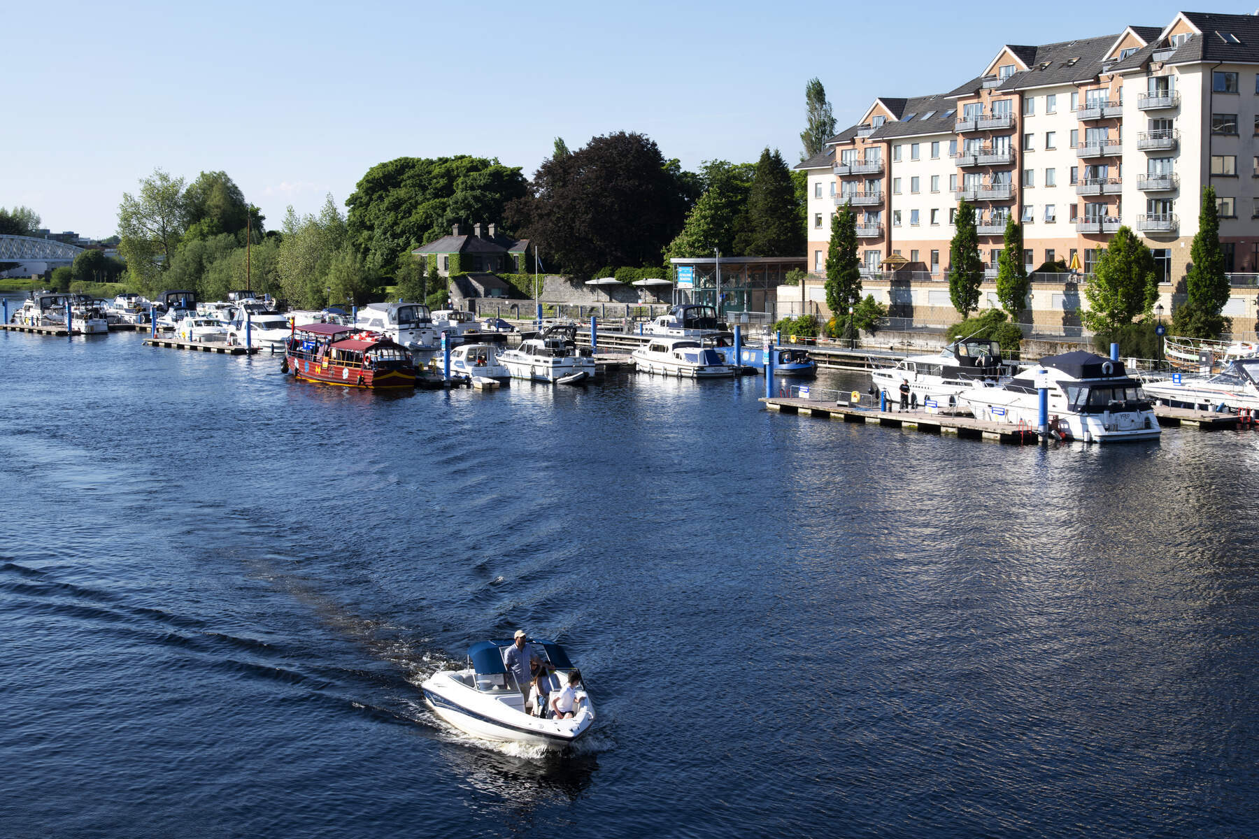 Boat on River Shannon near Radisson Blu Hotel Athlone with marina and waterfront buildings during a sunny day.